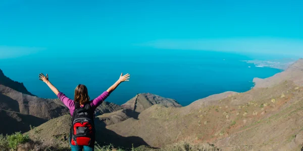 Mujer con los brazos extendidos de ruta en Canarias mirando hacia el mar