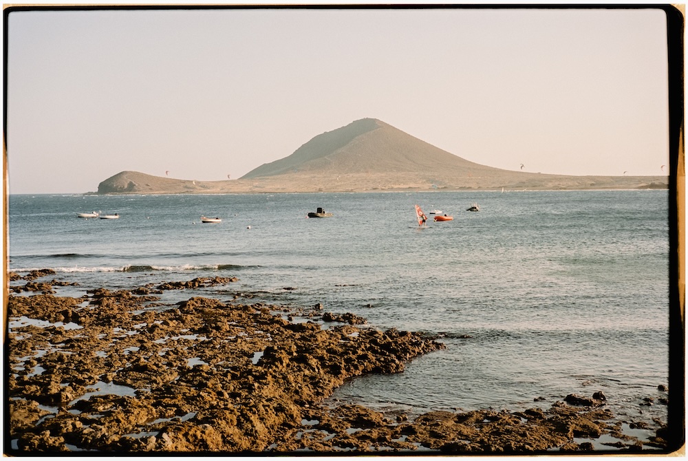 Playa de El Médano en Tenerife con arena volcánica, mar azul y la Montaña Roja al fondo.
