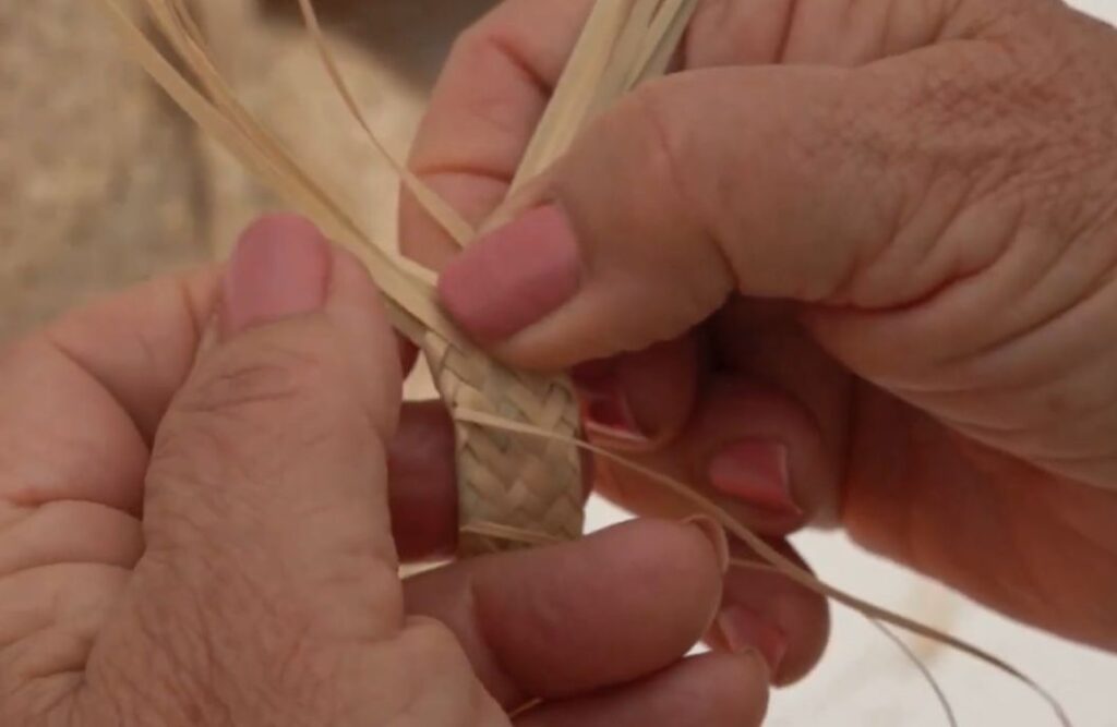 Primer plano de manos trenzando hojas de palmera seca en el proceso de elaboración de el sombrero gracioserito, de la isla de La Graciosa