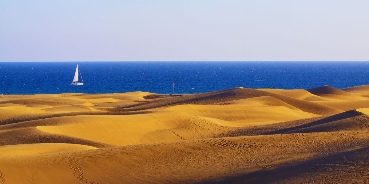 Vista de las dunas de Maspalomas con el mar al fondo y un barco navegando