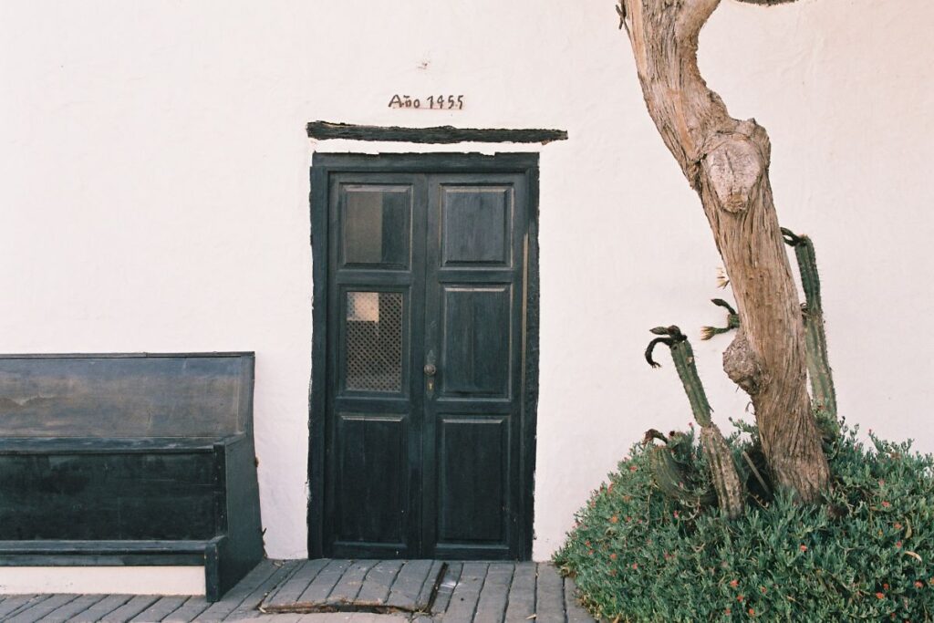 Puerta verde, banco y árbol frente a una fachada de Teguise
