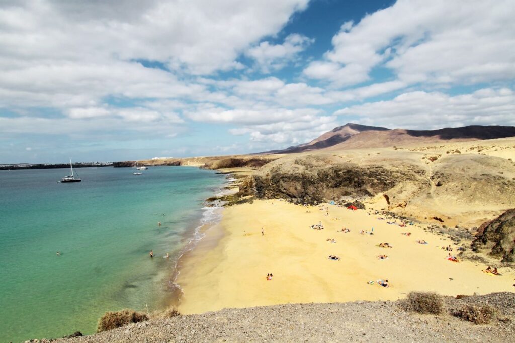 Vista de Playa Papagayo con visitantes tomando el sol y algunos barcos en el horizonte